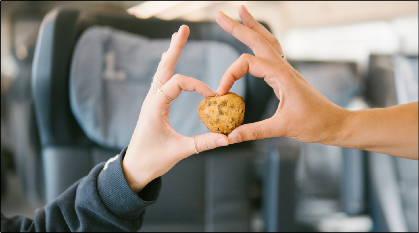Two hands form a heart around a heart-shaped cookie in a train compartment.